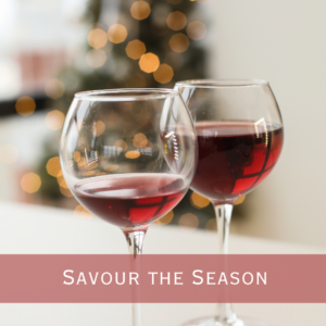 Two Red wines glasses in the forefront and a blurred image of a green pine Christmas tree decorated in the background.