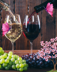 White and Red White being poured in wine glasses beside each other. Near the foot of the glasses are associate white and red grapes. 